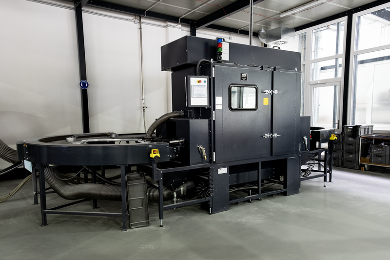 Große schwarze industrielle Durchlaufanlage mit Förderbändern und Kontrollpaneel in heller Produktionshalle mit Regalen und Lagerboxen
