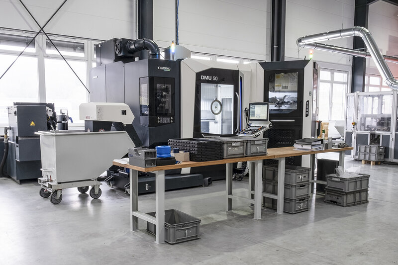Industrielle CNC-Maschine DMU 50 in einer Fertigungshalle mit Holztisch und Werkstattbehältern
