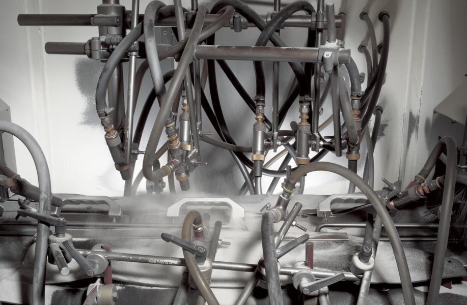 View into the blasting cabin of an automatic glass-ball blasting machine; aluminium handles in continuous blasting