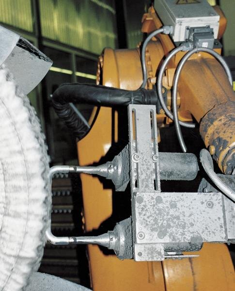 Ein orangefarbener industrieller Roboterarm mit mechanischer Vorrichtung behandelt ein Werkstück in einer Produktionsanlage