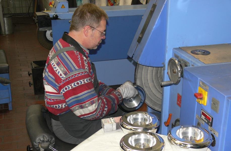 Mann bearbeitet metallische Werkstücke an einer blauen Schleifmaschine in einer Werkstatt