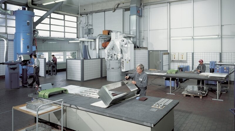 Industrielle Werkstatt mit Arbeitern, die metallische Bauteile bearbeiten an verschiedenen Maschinen und Werkbänken