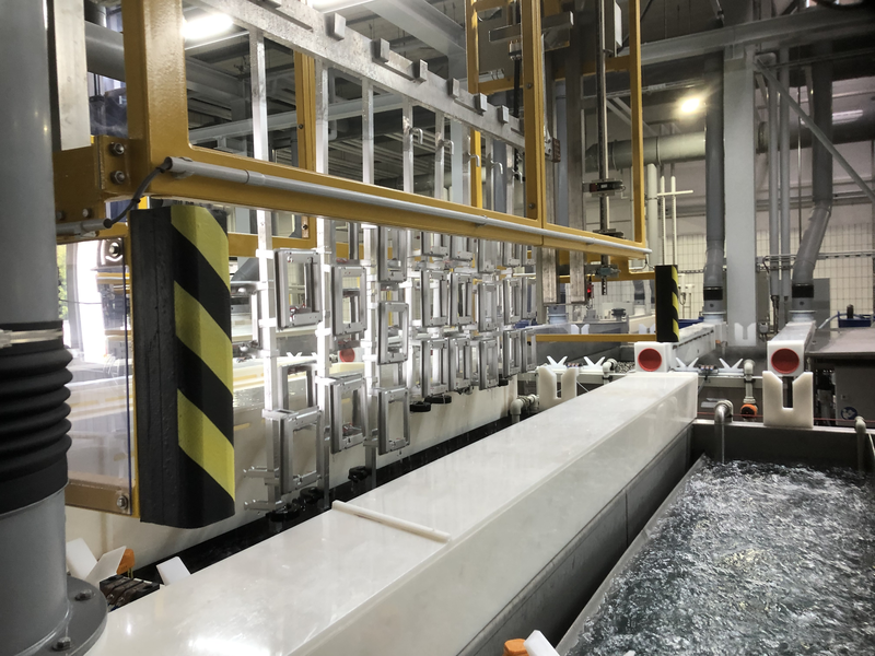 Industrielle Anlage mit aufgehängten Aluminiumrahmen über mehreren Flüssigkeitstanks in einer Produktionshalle