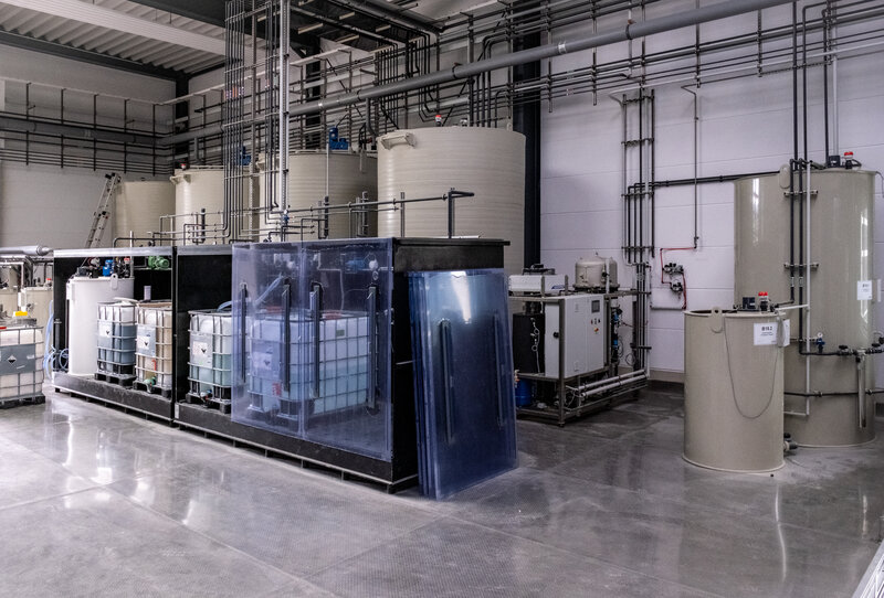 Mehrere große zylindrische Lagertanks und Containerbehälter in einer sauberen Industriehalle mit Rohrleitungen und technischer Ausrüstung