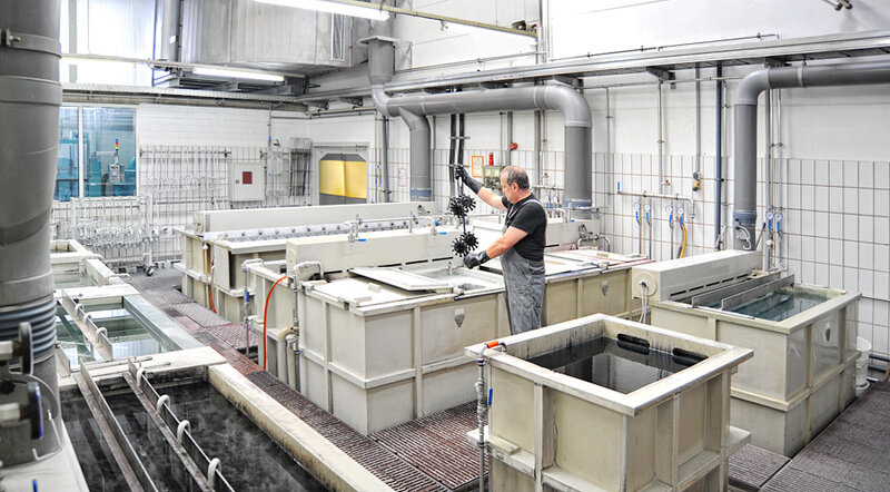 Mann in industriellem Raum arbeitet an Bauteil über großer rechteckiger Wanne mit technischen Anlagen im Hintergrund