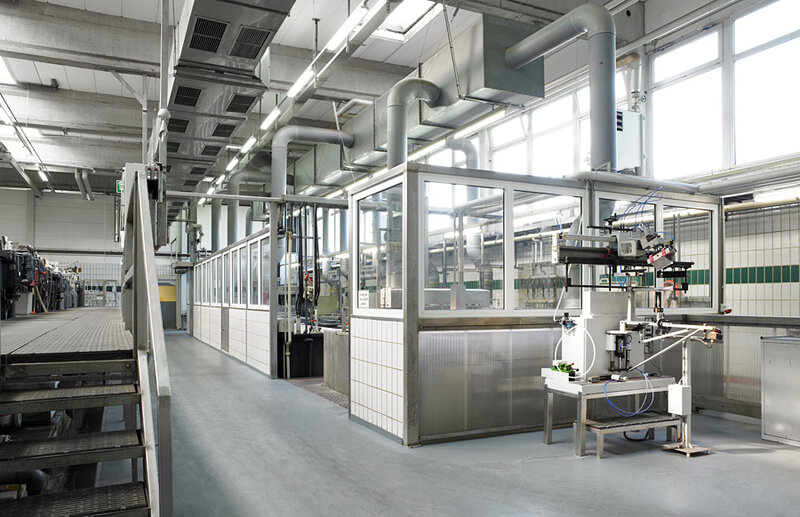 Industrielle Produktionshalle mit Glasabtrennung, Lüftungsrohren an der Decke und einer komplexen Maschine auf dem Boden