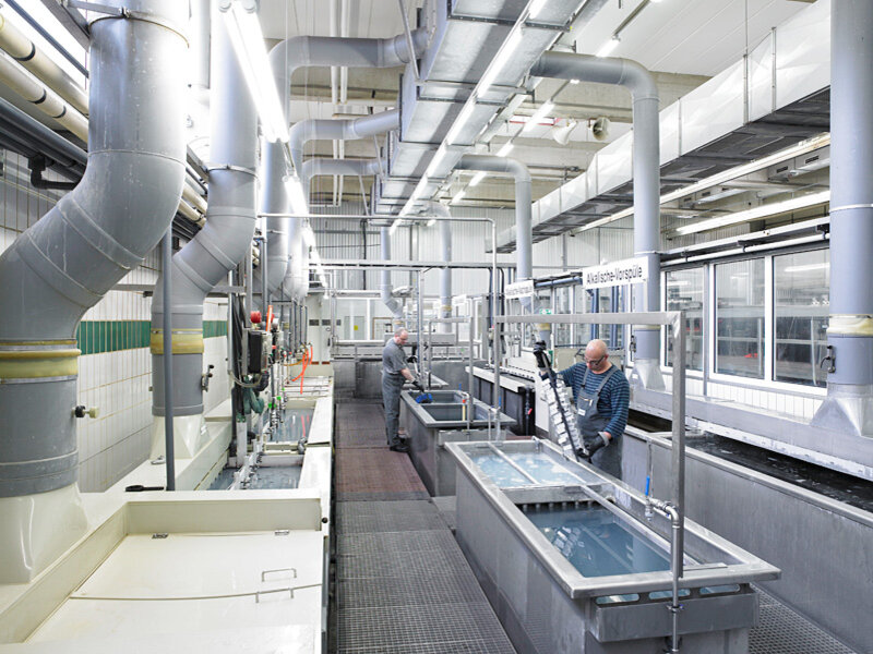Industrieller Waschraum mit großen Edelstahlwaschanlagen und zwei Männern, die metallene Teile reinigen