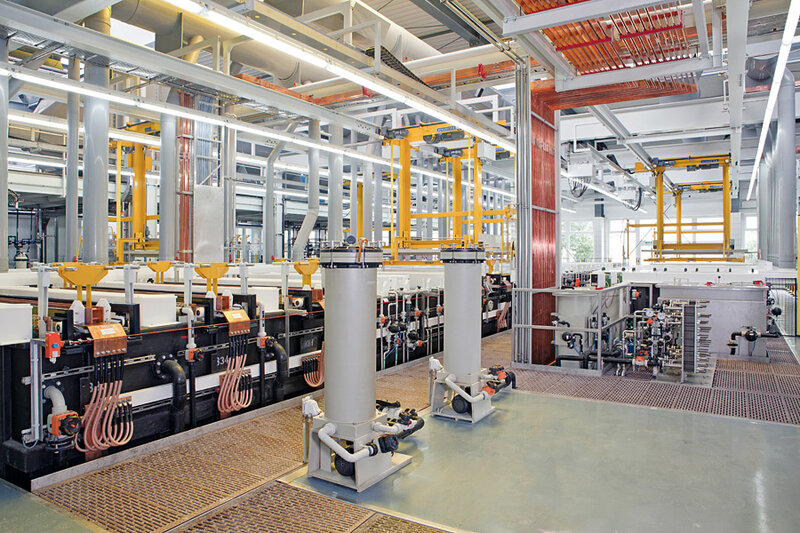 Innenansicht einer Industrielackieranlage mit vertikalen Rohren, Hebevorrichtungen und technischen Komponenten auf einem Gitterboden