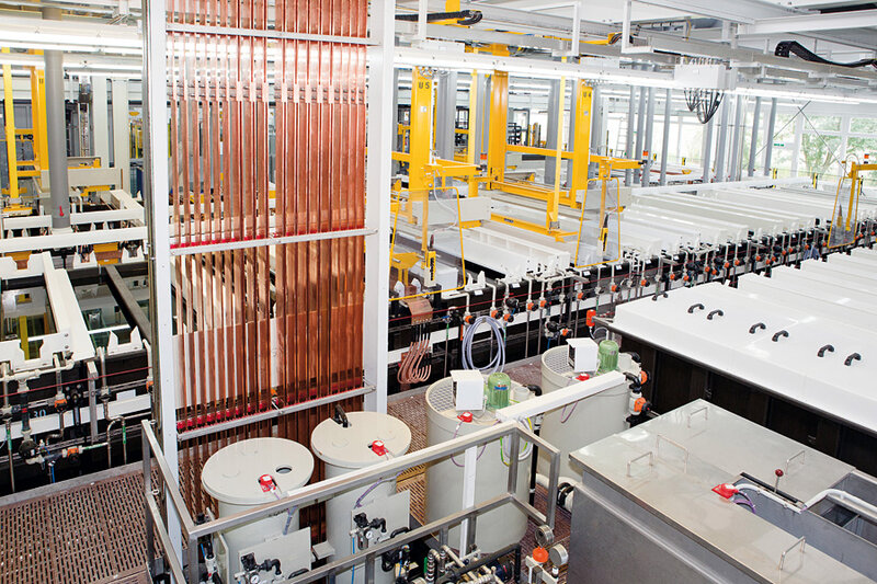 Industrielle Fertigungsanlage mit vertikalen Kupferplatten, mehreren Tanks und weißen Becken in einer hellen Fabrikhalle