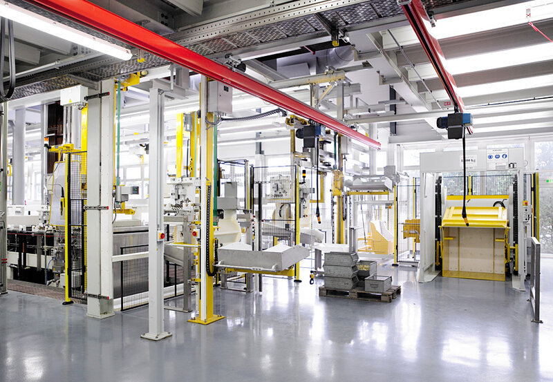 Moderne Industrieanlage mit gelben und roten Hebevorrichtungen und Maschinen in einer gut beleuchteten Halle mit glänzendem Boden