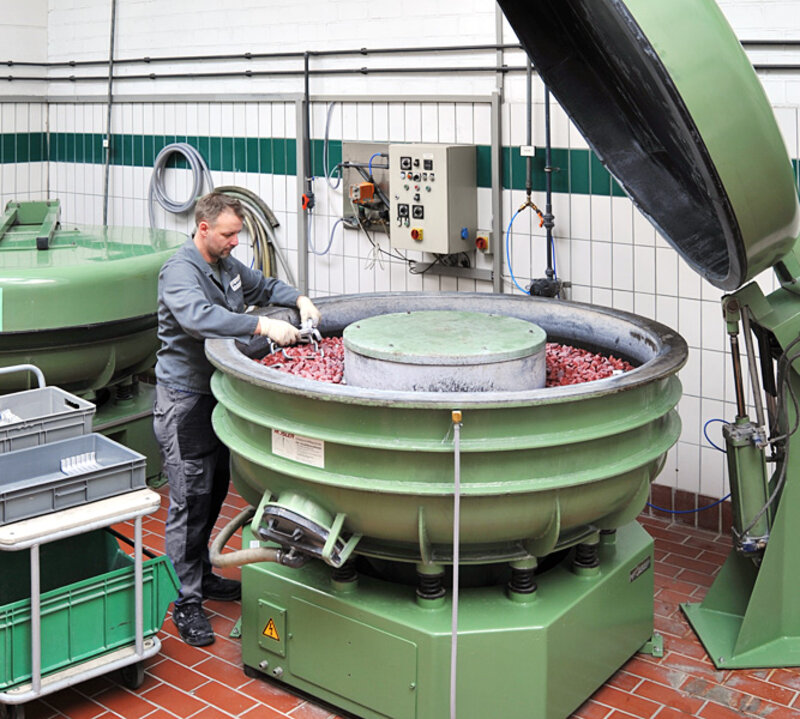 Mann in Arbeitskleidung arbeitet an großer grün lackierter Trommelmaschine mit roten Komponenten in gefliestem Fabrikraum