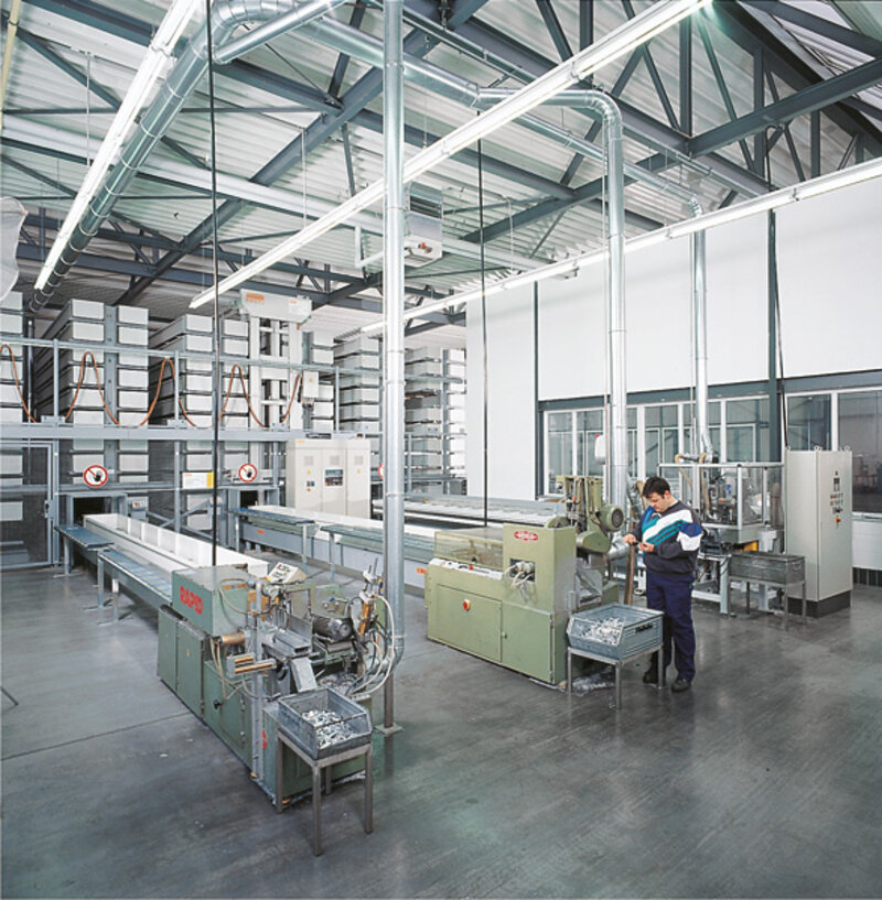 Innenansicht einer Produktionshalle mit Maschinen und einem Arbeiter, der an einer Maschine arbeitet