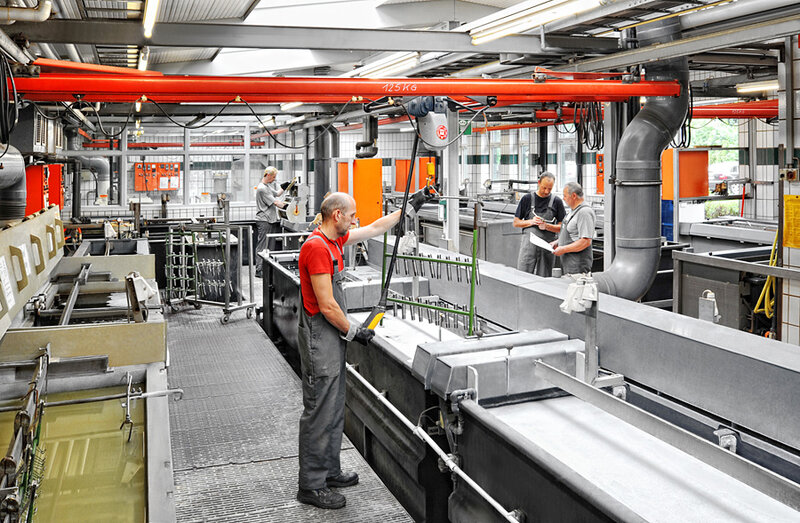 Industrielle Produktionshalle mit vier Arbeitern, die Metallteile in großen Metallwannen verarbeiten