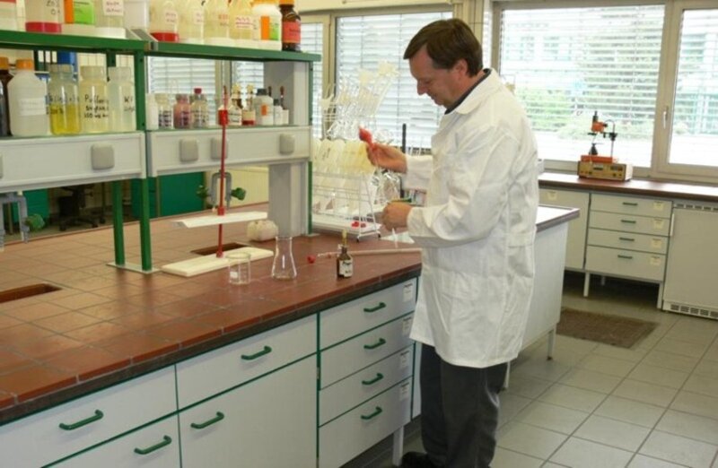 Mann in weißem Laborkittel arbeitet mit Pipette an Laborarbeitstheke mit Chemikalien und Laborgeräten